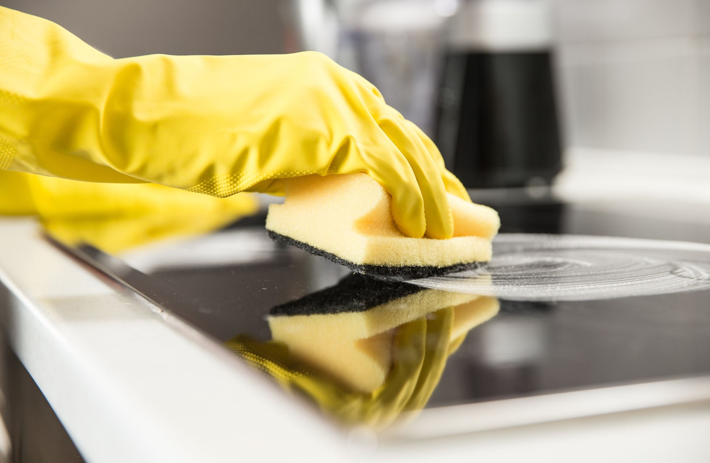 hand in yellow gloves using induction hob cleaner